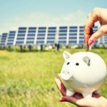 Solar penny stocks: Piggy bank in front of solar panel infrastructure